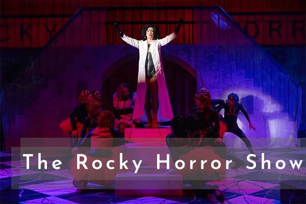 Image of a scene from Colorado State University's 2021 production of The Rocky Horror show. Frank standing on a box as ensemble fawns over him.